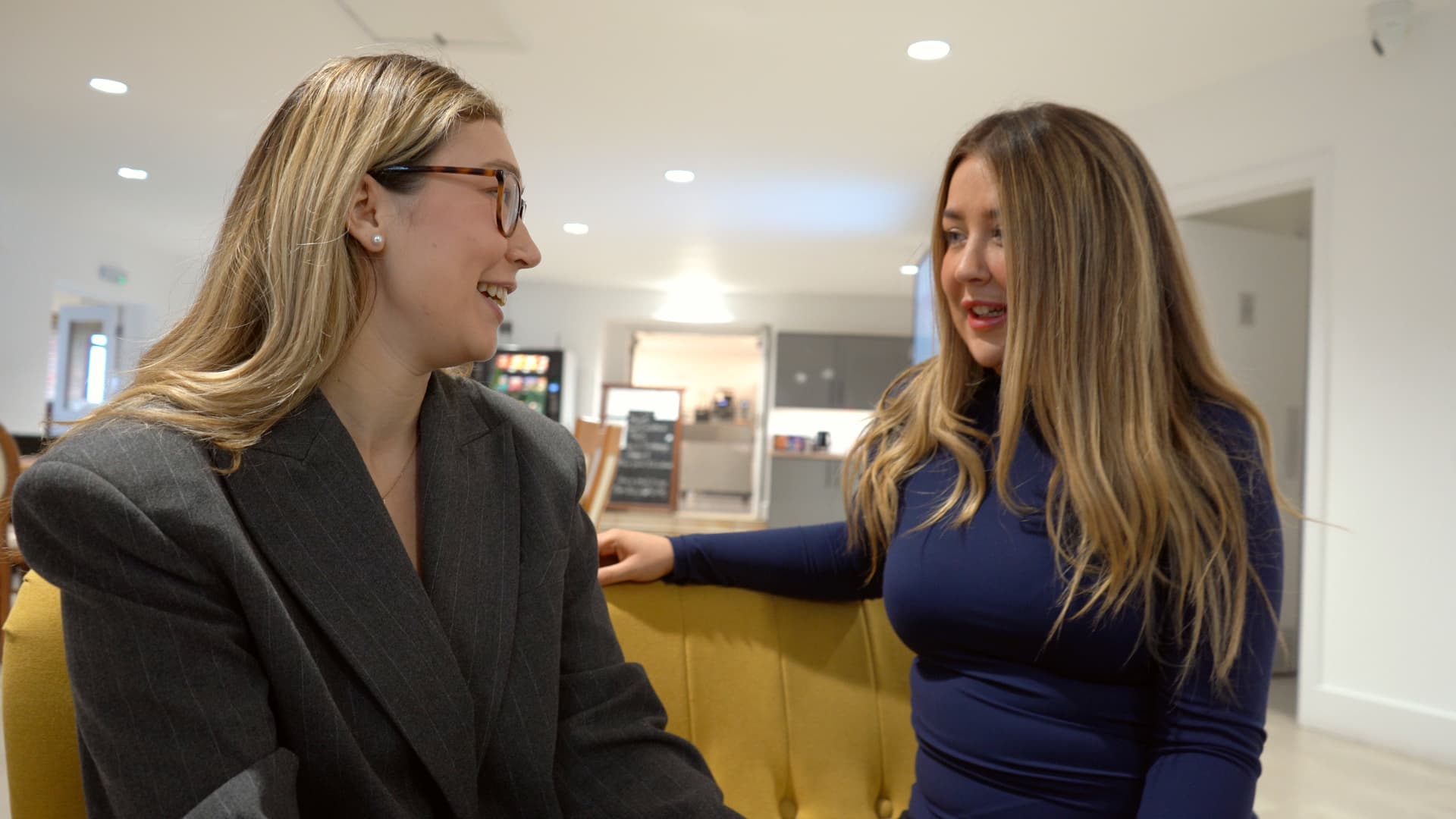 Two colleagues laughing together in the bright office breakout area